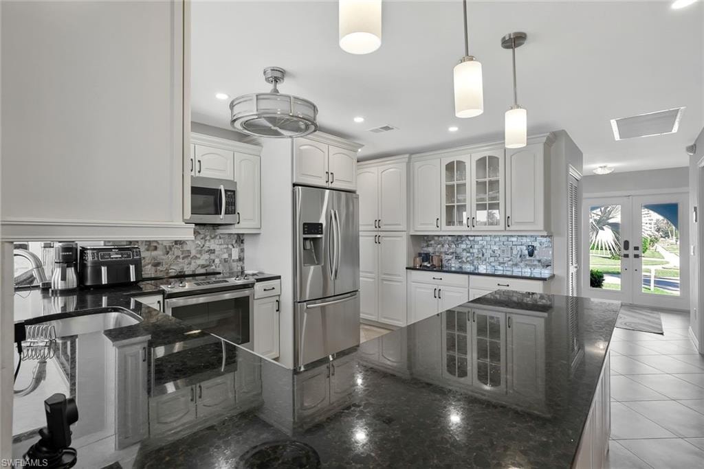Kitchen with dark stone countertops, stainless steel appliances, glass insert cabinets, backsplash, and white cabinets