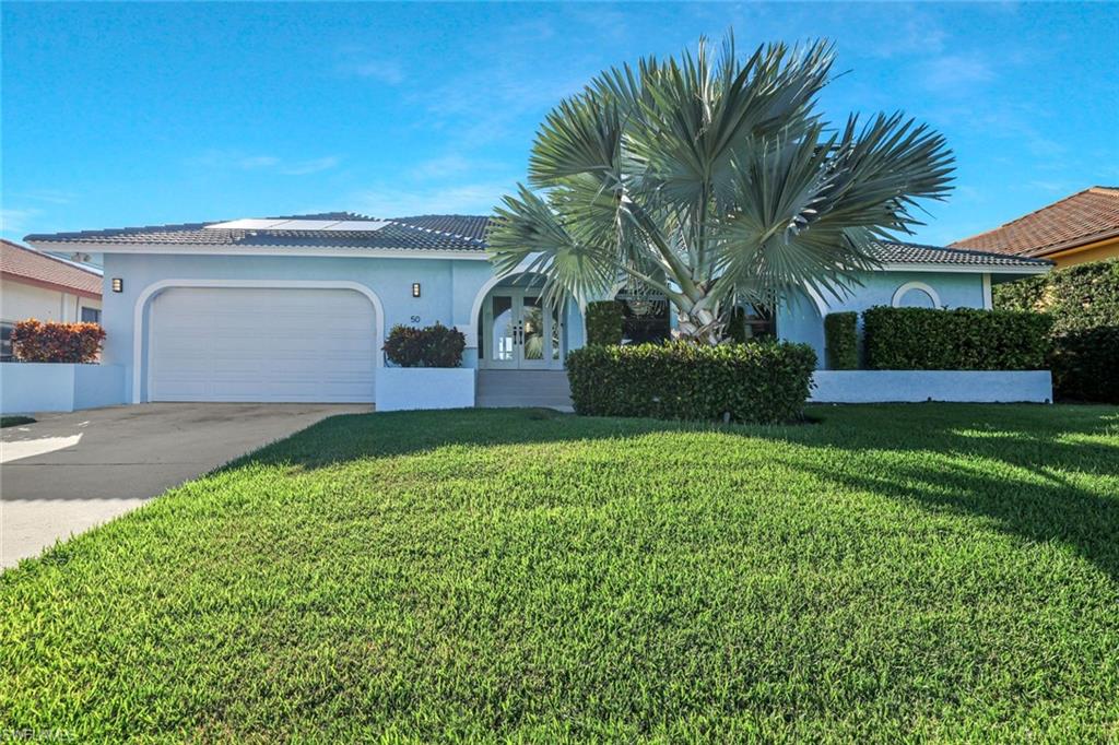 View of front facade featuring stucco siding, driveway, a garage, and a front yard