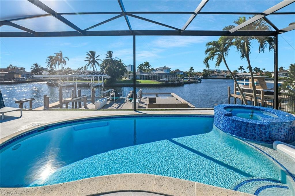 View of swimming pool with a water view, boat lift, a pool with connected hot tub, a boat dock, and glass enclosure