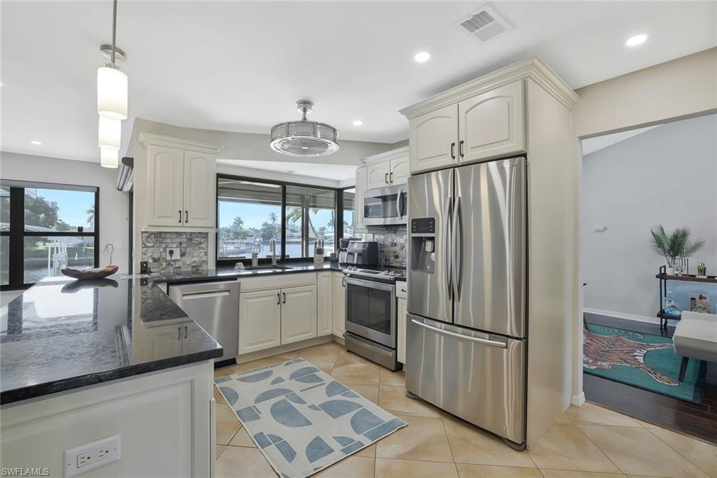 Kitchen with stainless steel appliances, dark stone counters, light tile patterned flooring, decorative light fixtures, and tasteful backsplash