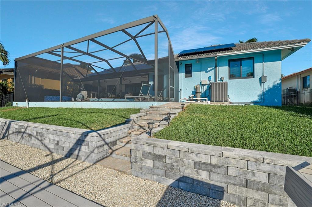 Back of property with a lawn, a sunroom, glass enclosure, and roof mounted solar panels