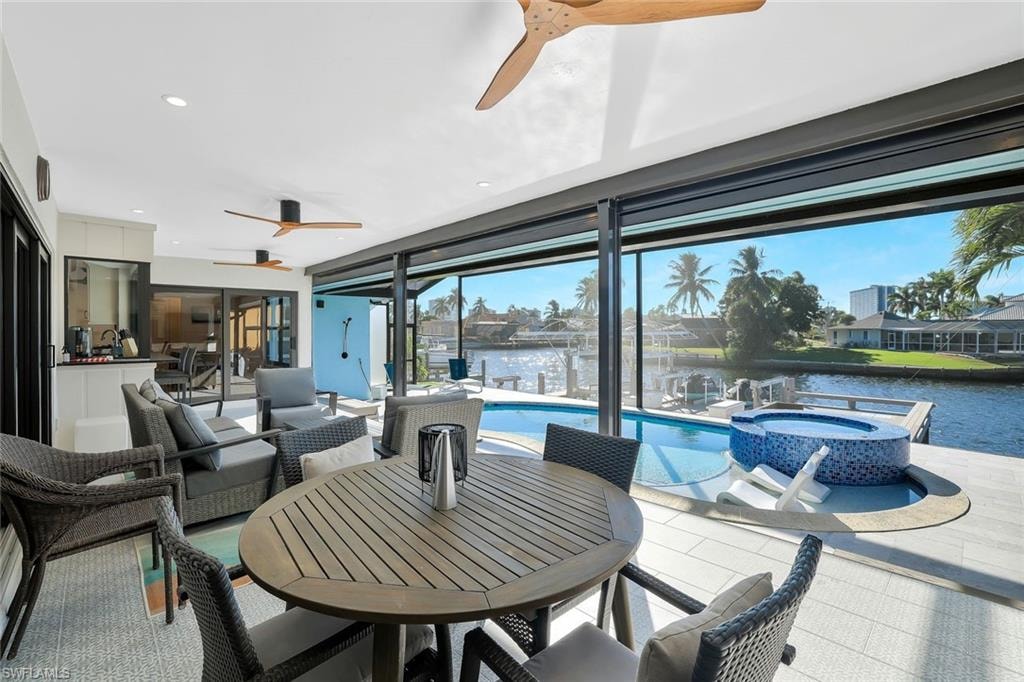 View of patio featuring ceiling fan, outdoor dining space, a pool with connected hot tub, a water view, and an outdoor living space