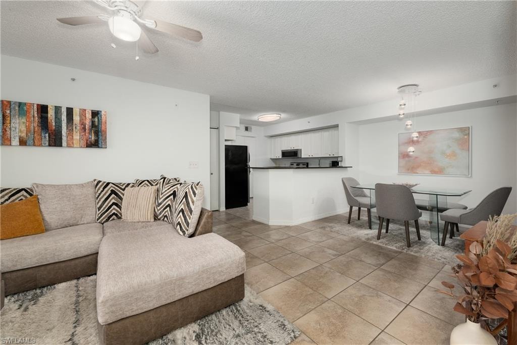 Living room featuring a textured ceiling, light tile patterned flooring, and ceiling fan