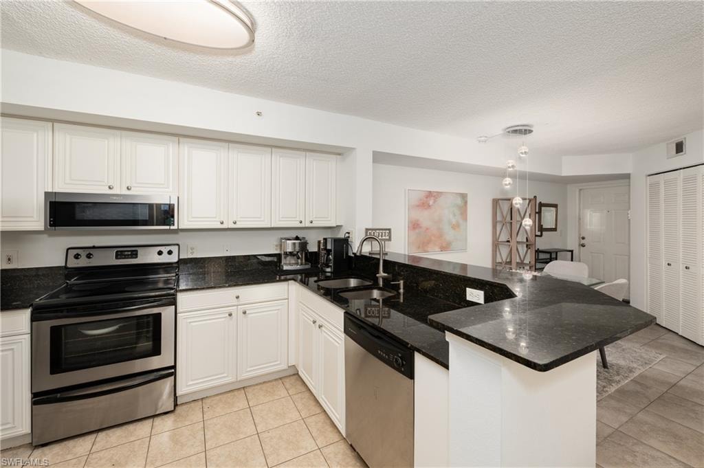 Kitchen with appliances with stainless steel finishes, a textured ceiling, dark stone counters, a peninsula, and white cabinets