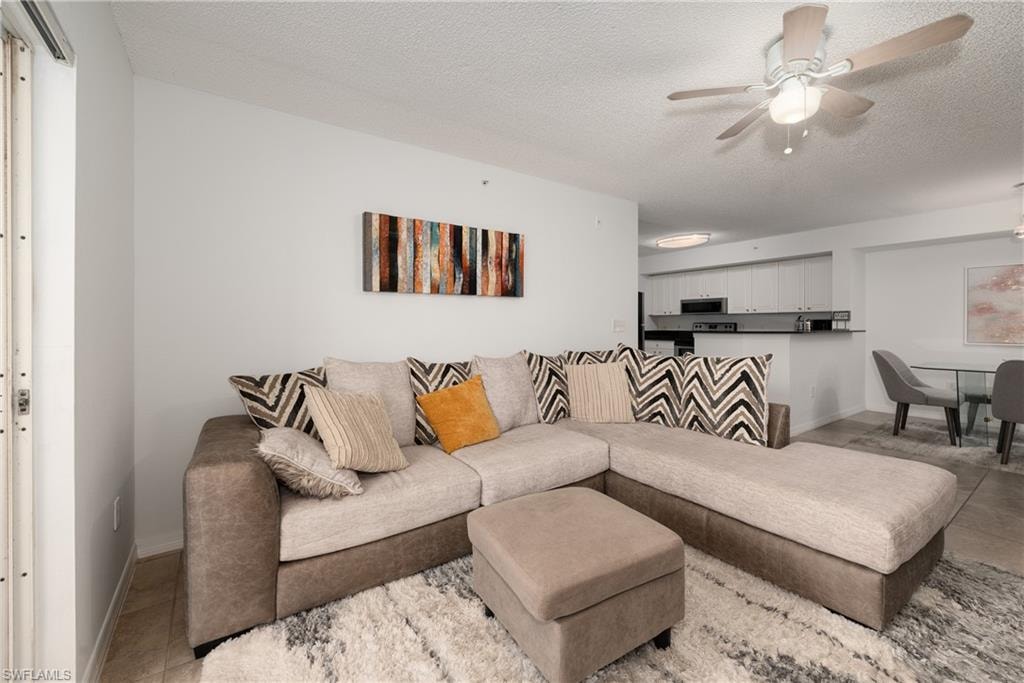 Living room with light tile patterned flooring, a ceiling fan, and a textured ceiling