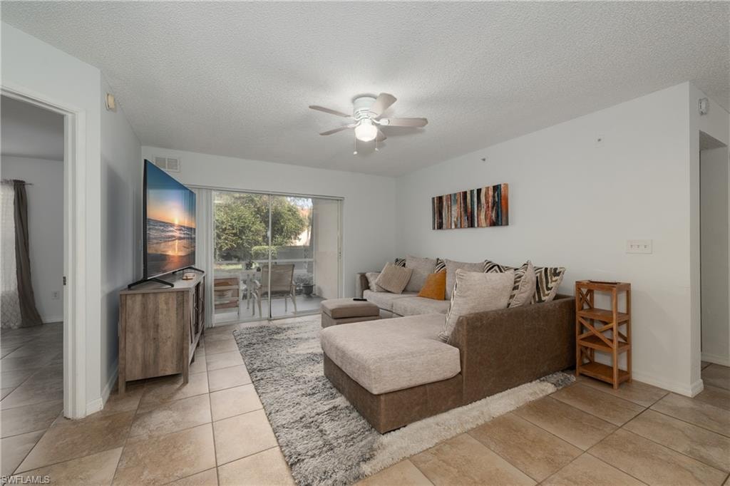 Living room with ceiling fan, a textured ceiling, and light tile patterned floors