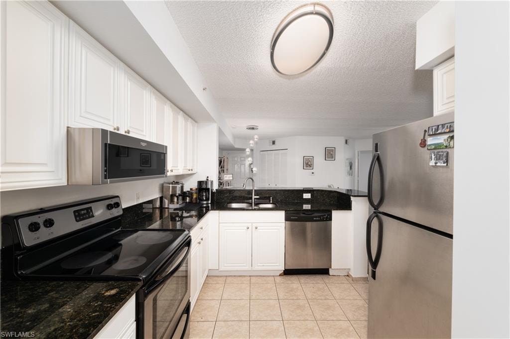 Kitchen with appliances with stainless steel finishes, a textured ceiling, light tile patterned floors, white cabinets, and dark stone countertops