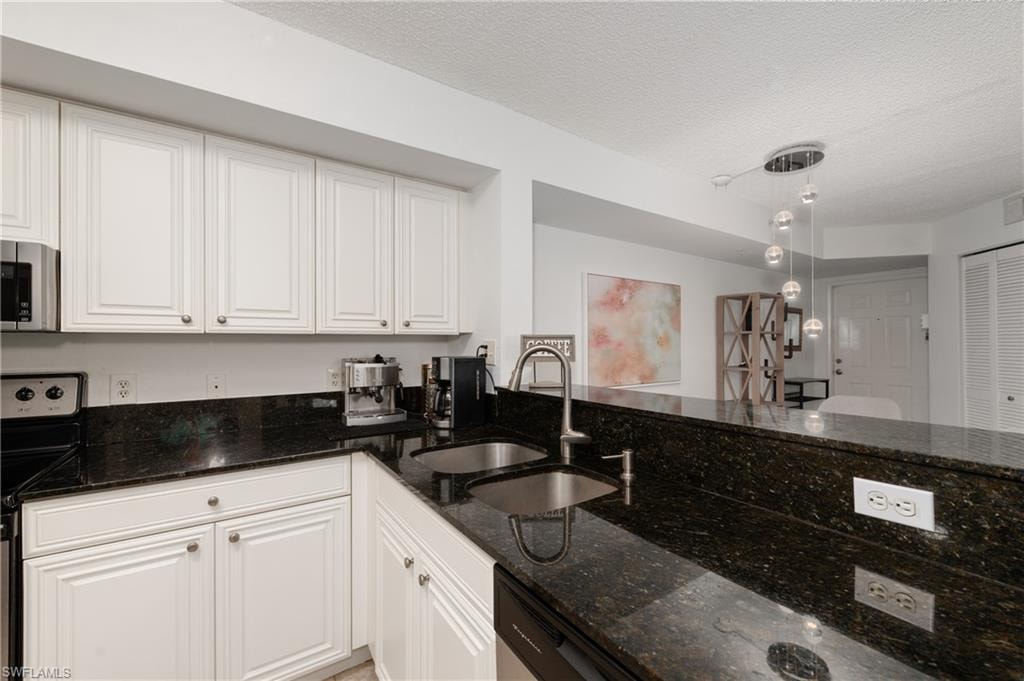 Kitchen featuring dark stone countertops, appliances with stainless steel finishes, white cabinets, and a textured ceiling