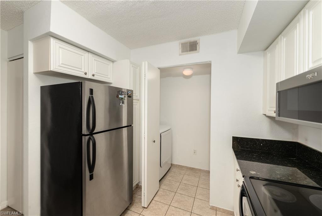 Kitchen with stainless steel appliances, light tile patterned floors, white cabinets, a textured ceiling, and dark stone counters
