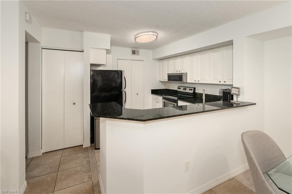 Kitchen featuring stainless steel appliances, dark stone counters, a peninsula, a textured ceiling, and light tile patterned flooring