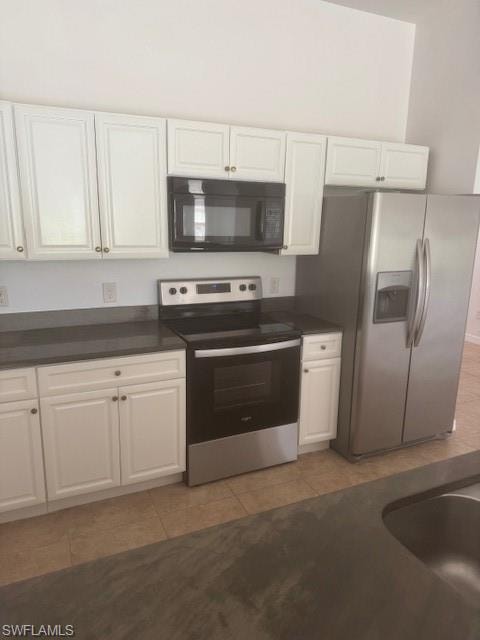 Kitchen with dark countertops, electric range oven, white cabinetry, and fridge