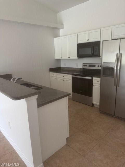 Kitchen featuring dark countertops, refrigerator, range, and white cabinetry