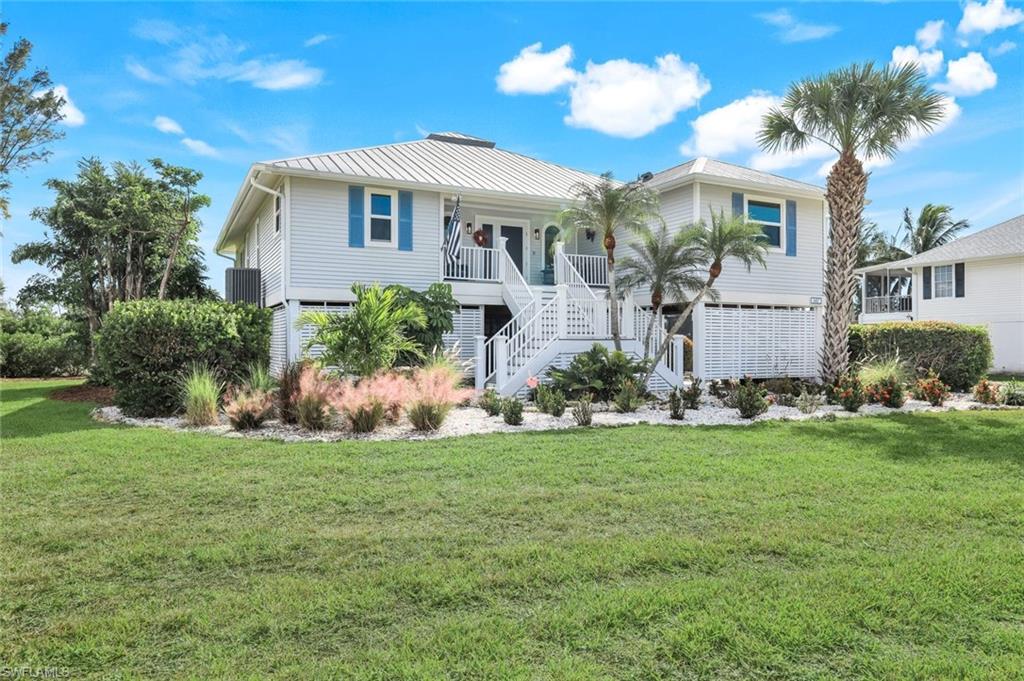 Beach home with stairway, a front yard, and a metal roof
