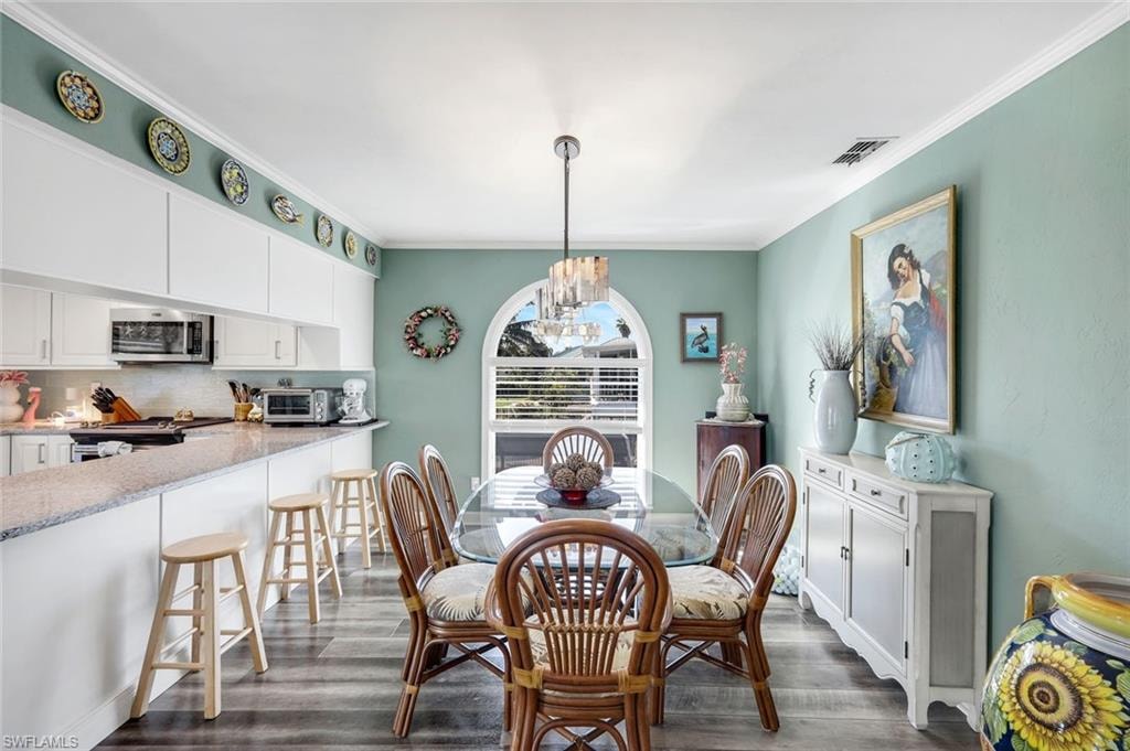 Dining area featuring a chandelier, crown molding, and dark wood-style flooring