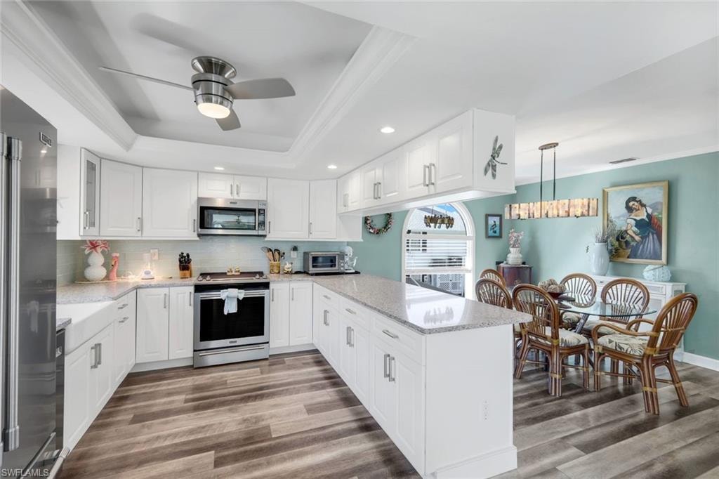 Kitchen featuring backsplash, light stone counters, a raised ceiling, ornamental molding, and appliances with stainless steel finishes