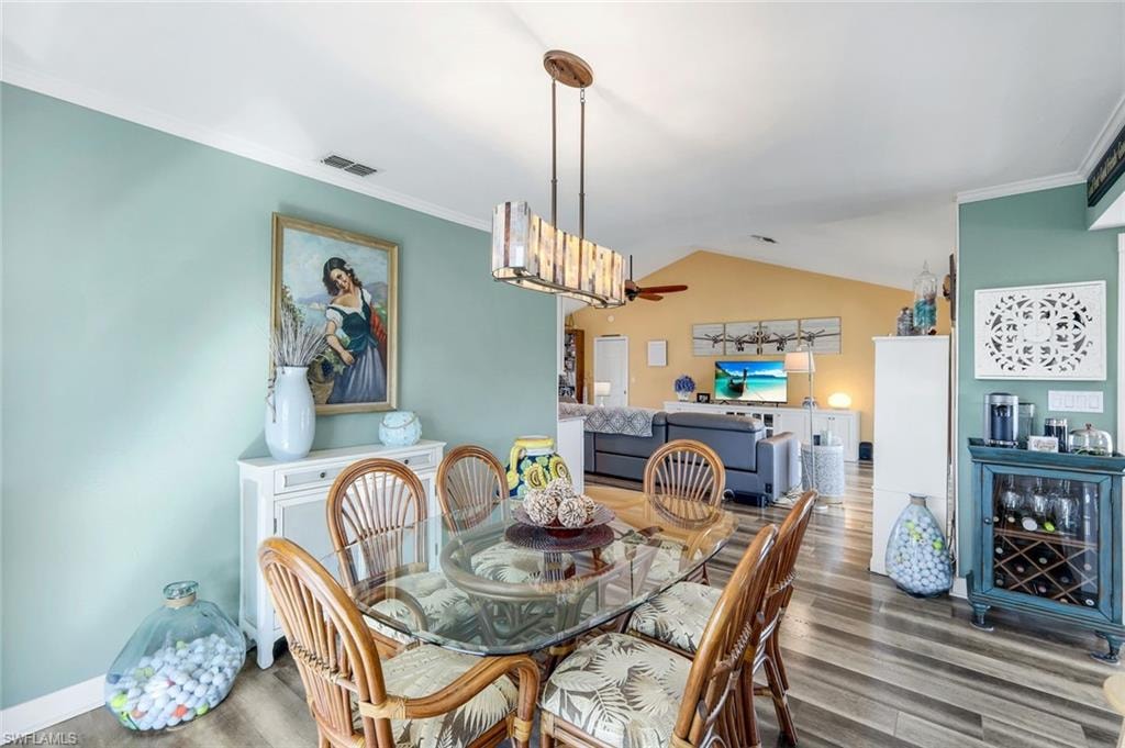 Dining space with crown molding, wood finished floors, lofted ceiling, and ceiling fan