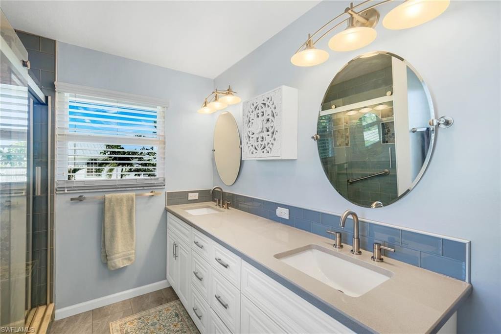 Full bath featuring double vanity, a stall shower, and decorative backsplash