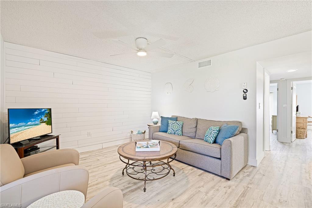 Living room with wood finished floors, a textured ceiling, ceiling fan, and wood walls