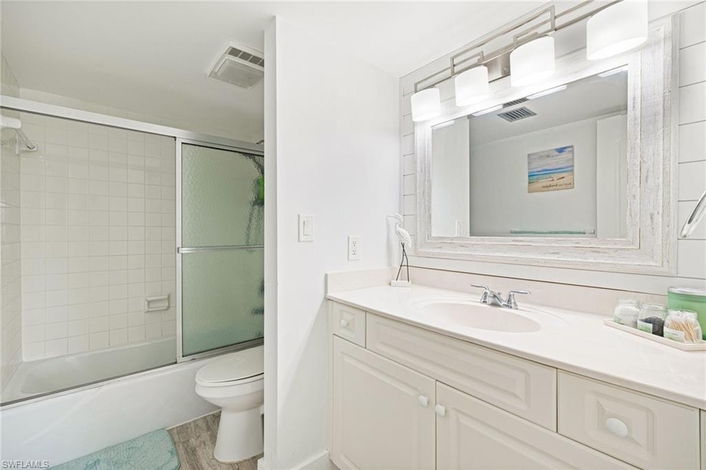 Full bathroom with vanity, enclosed tub / shower combo, and light wood finished floors