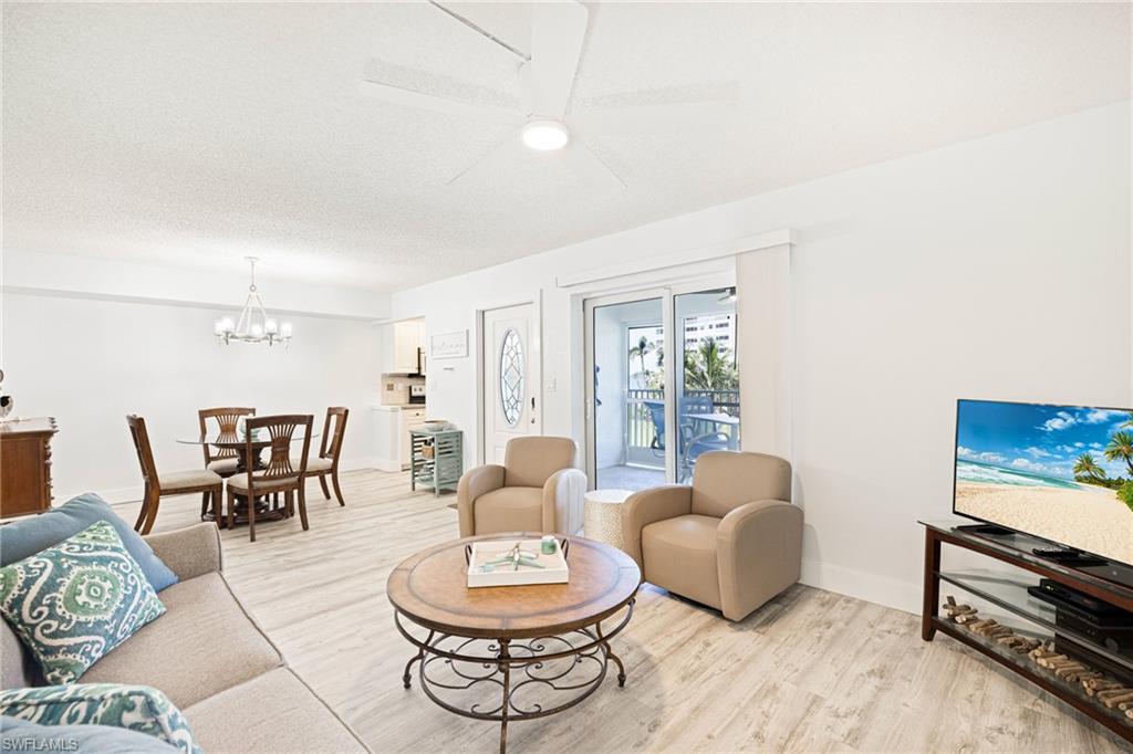 Living area featuring light wood-style flooring, a ceiling fan, a chandelier, and a textured ceiling