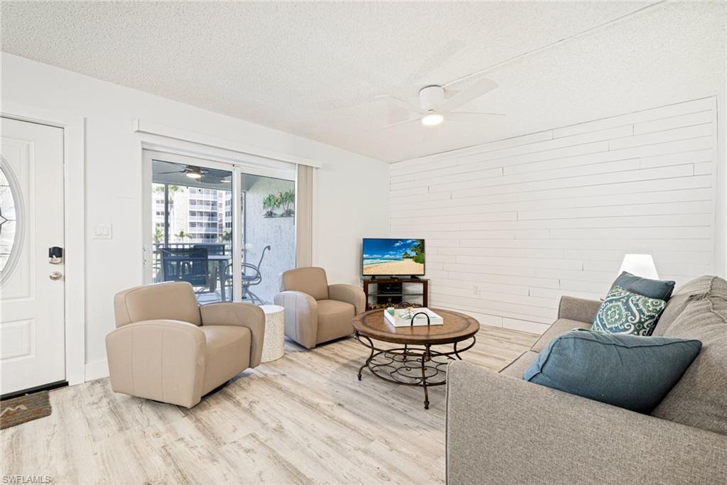 Living area with a textured ceiling, wood finished floors, wooden walls, and ceiling fan