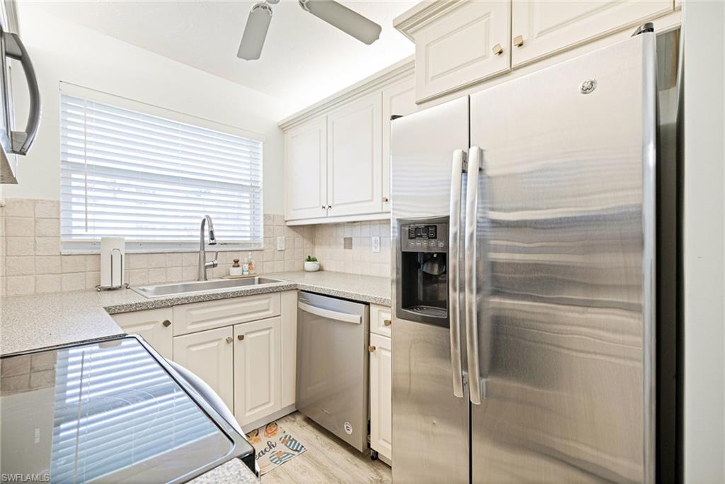 Kitchen with appliances with stainless steel finishes, tasteful backsplash, white cabinets, light wood finished floors, and light stone countertops