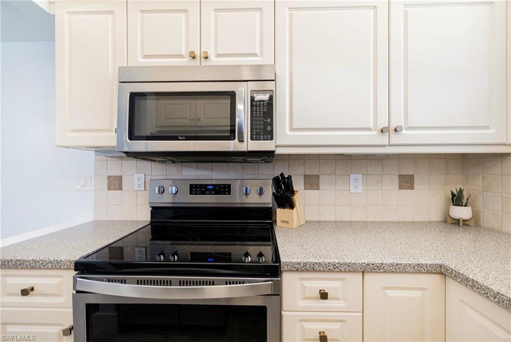 Kitchen featuring stainless steel appliances, decorative backsplash, light stone counters, and white cabinetry