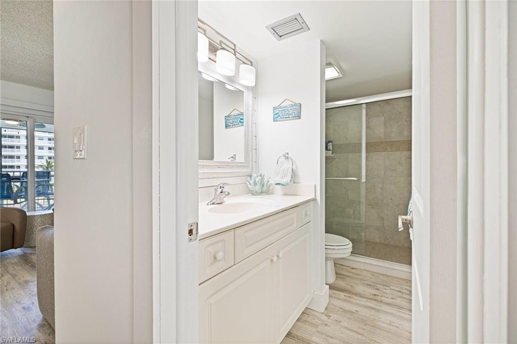 Full bathroom featuring light wood-style flooring, a shower stall, vanity, and a textured ceiling