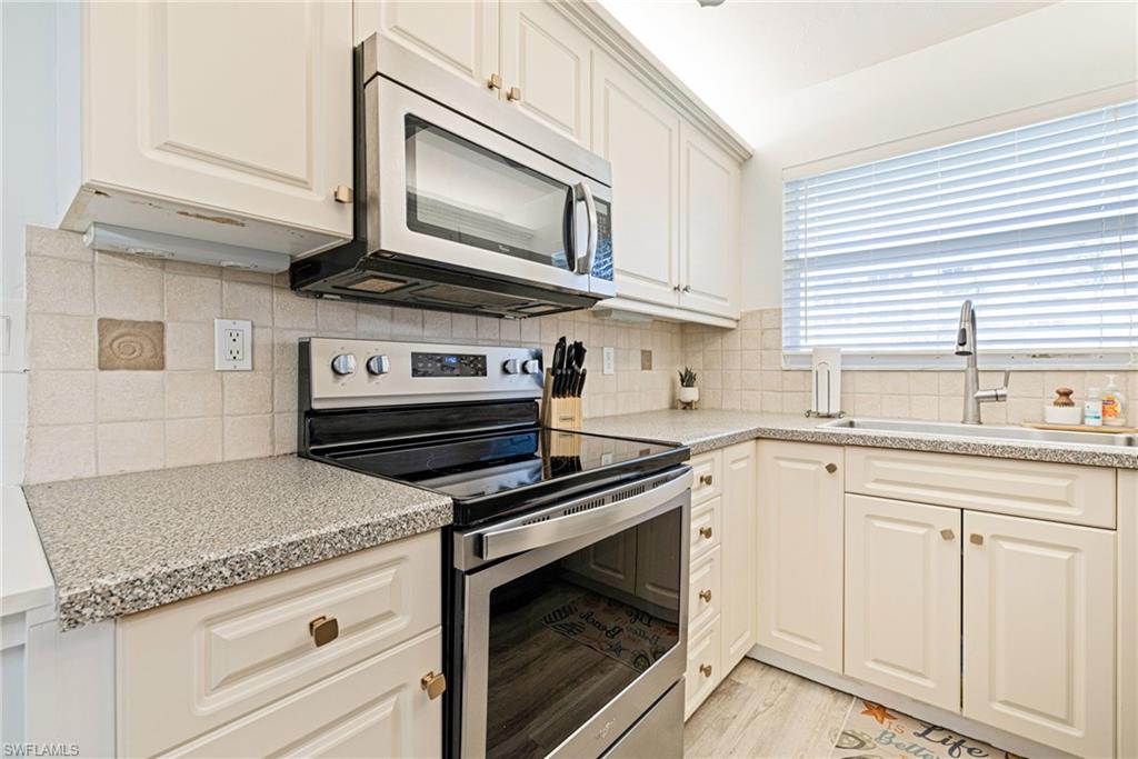 Kitchen featuring stainless steel appliances, decorative backsplash, light stone countertops, white cabinetry, and light wood-type flooring