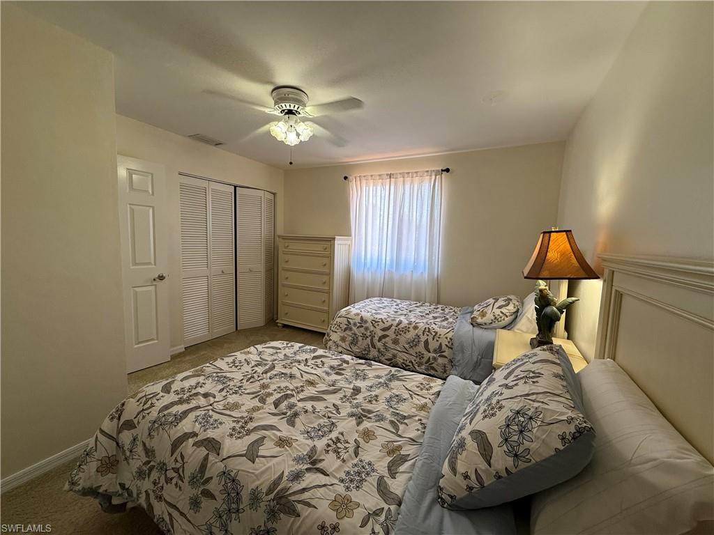 Carpeted bedroom with ceiling fan and a closet