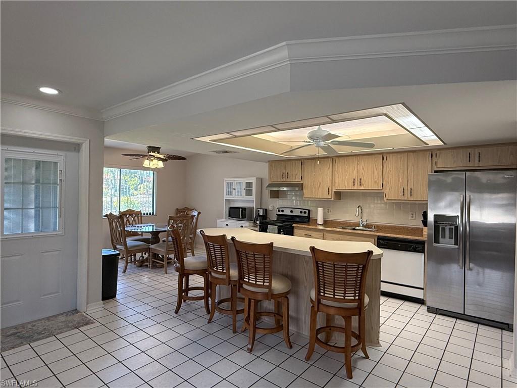 Kitchen featuring stainless steel appliances, decorative backsplash, a breakfast bar area, light tile patterned floors, and crown molding