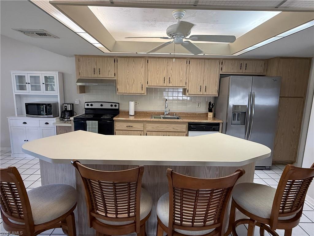 Kitchen featuring light tile patterned flooring, a kitchen bar, light countertops, appliances with stainless steel finishes, and a kitchen island