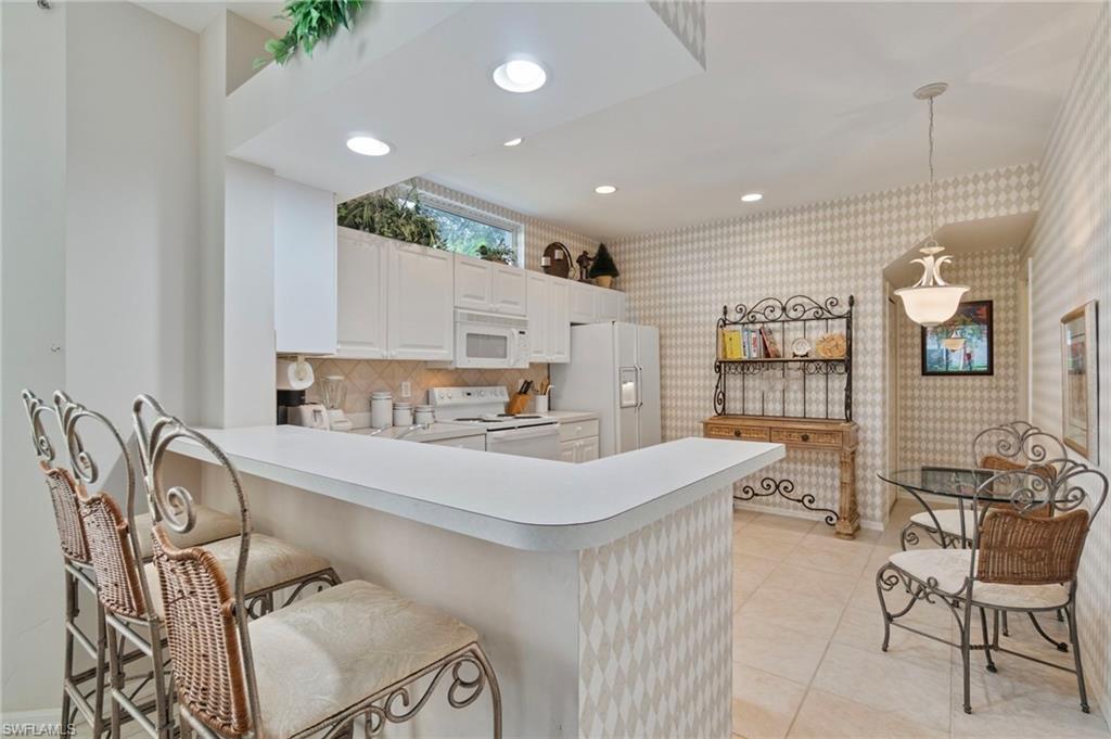 Kitchen with recessed lighting, light countertops, white appliances, decorative light fixtures, and a peninsula