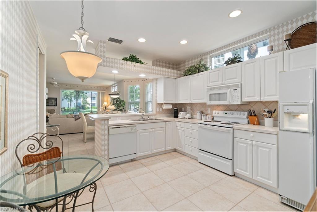 Kitchen with decorative backsplash, white appliances, hanging light fixtures, light countertops, and open floor plan