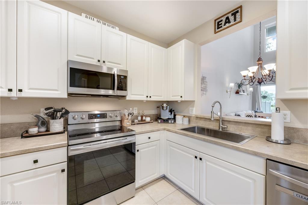 Kitchen with appliances with stainless steel finishes, a chandelier, white cabinets, light tile patterned floors, and hanging light fixtures