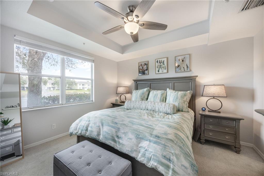 Bedroom with a tray ceiling, light colored carpet, and a ceiling fan
