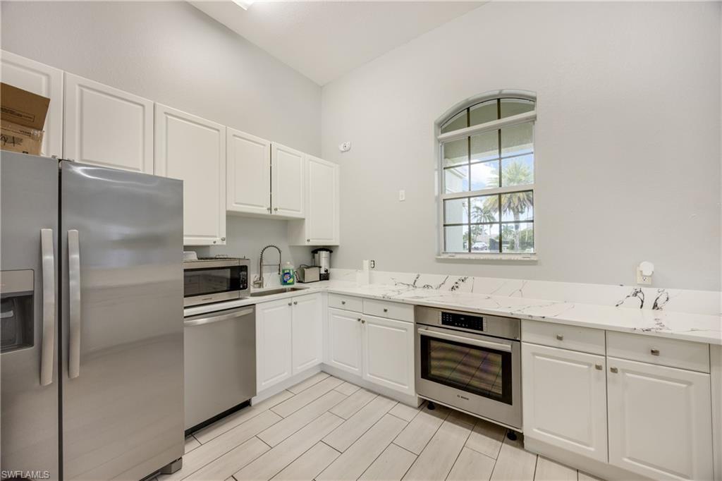 Kitchen with appliances with stainless steel finishes, white cabinetry, and light stone countertops