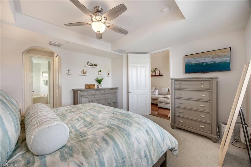 Bedroom featuring ensuite bathroom, arched walkways, carpet flooring, and a ceiling fan
