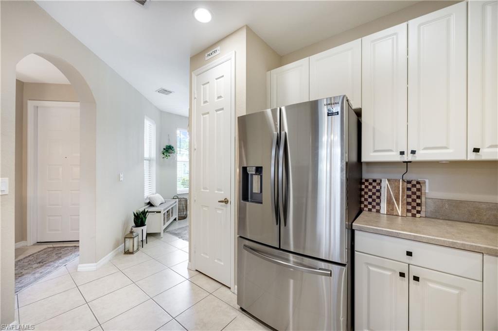 Kitchen featuring stainless steel refrigerator with ice dispenser, light countertops, arched walkways, white cabinetry, and light tile patterned floors