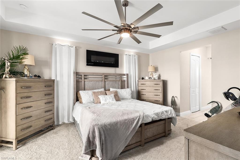 Owners suite with light carpet, ceiling fan, and  tray ceiling
