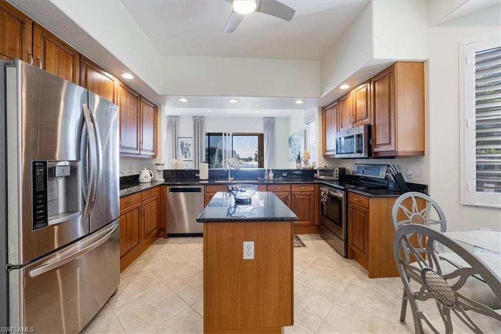Kitchen with stainless steel appliances, brown cabinets, a kitchen island, dark stone counters, and plenty of natural light