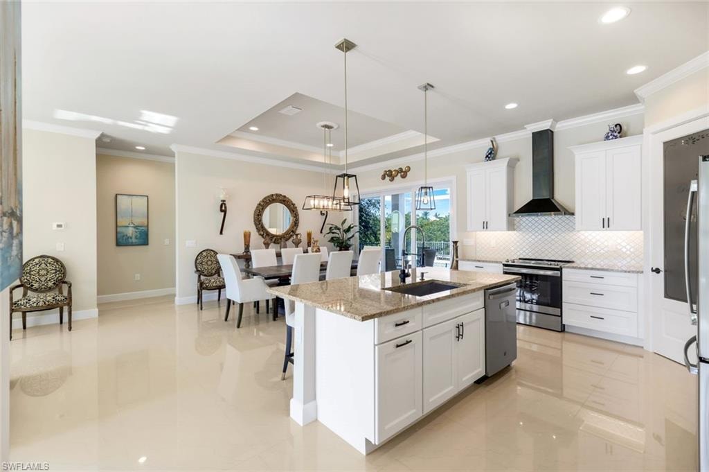 Kitchen with ornamental molding, stainless steel appliances, a raised ceiling, white cabinets, and pendant lighting