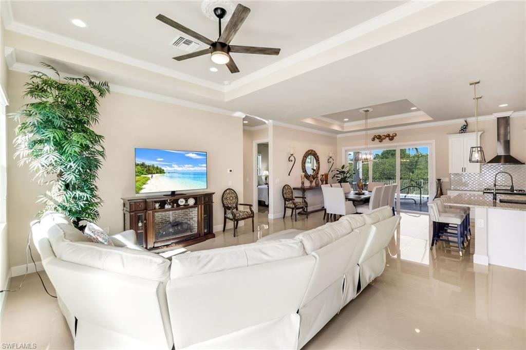 Living room with a tray ceiling, crown molding, recessed lighting, ceiling fan, and light tile patterned floors
