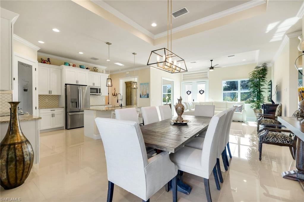 Dining space with crown molding, a tray ceiling, recessed lighting, light tile patterned flooring, and a chandelier