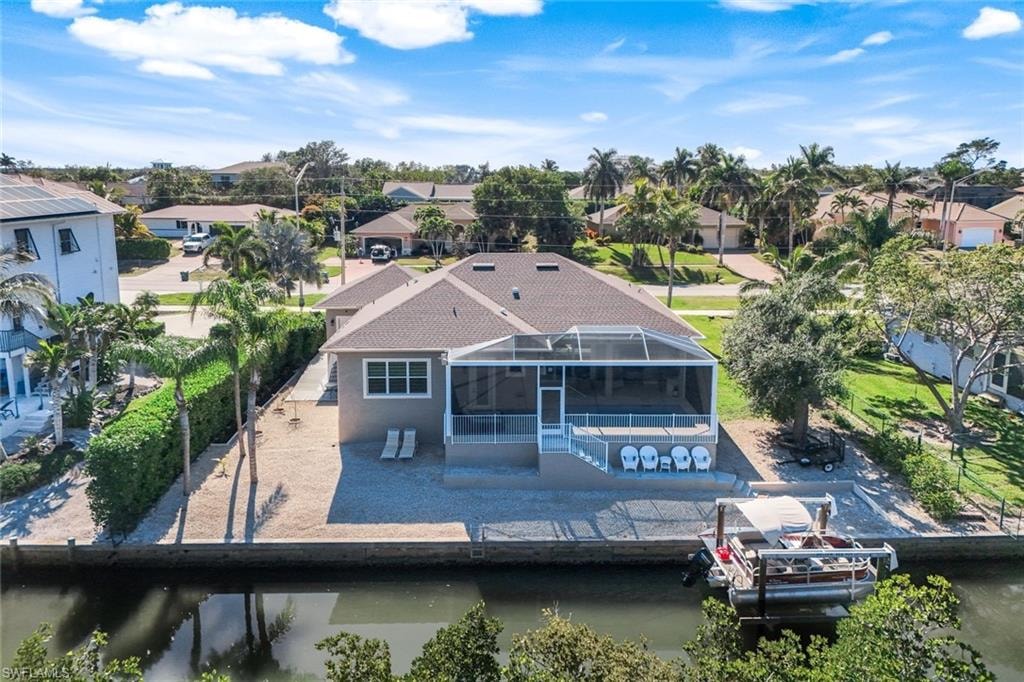 Rear view of property featuring a residential view, a water view, a sunroom, and glass enclosure