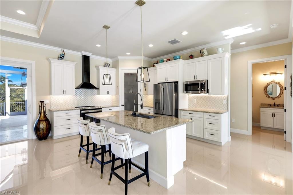 Kitchen featuring crown molding, a breakfast bar, white cabinets, appliances with stainless steel finishes, and light stone counters