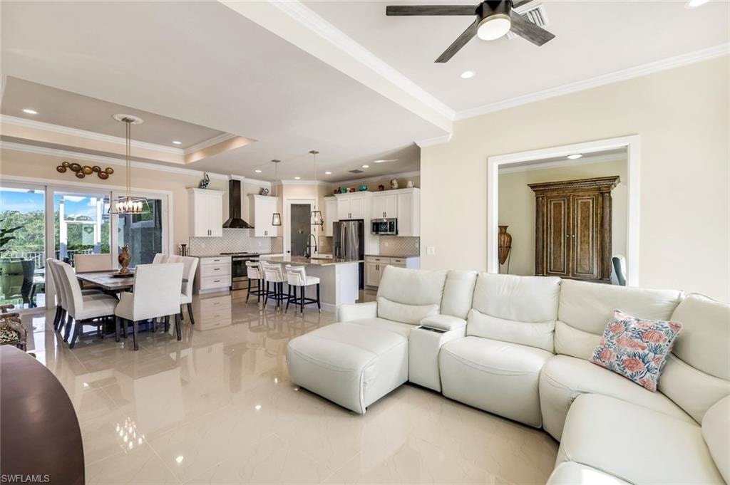 Living area with crown molding, a tray ceiling, recessed lighting, a chandelier, and a ceiling fan
