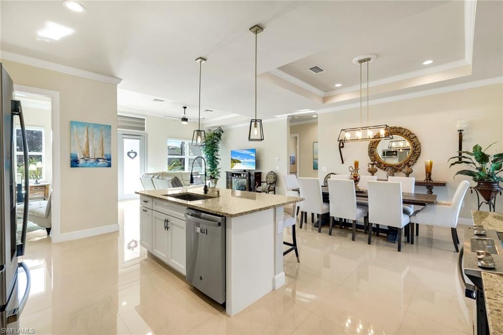 Kitchen featuring ornamental molding, light stone countertops, an island with sink, decorative light fixtures, and recessed lighting