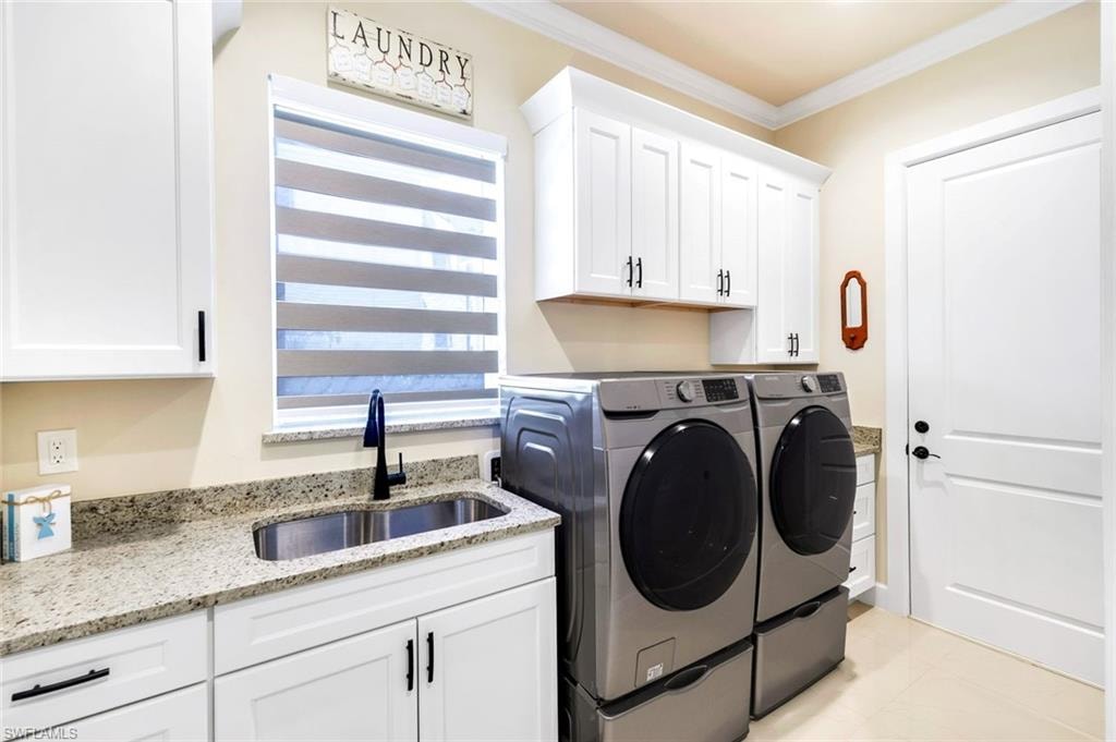 Washroom with ornamental molding, separate washer and dryer, cabinet space, and light tile patterned flooring