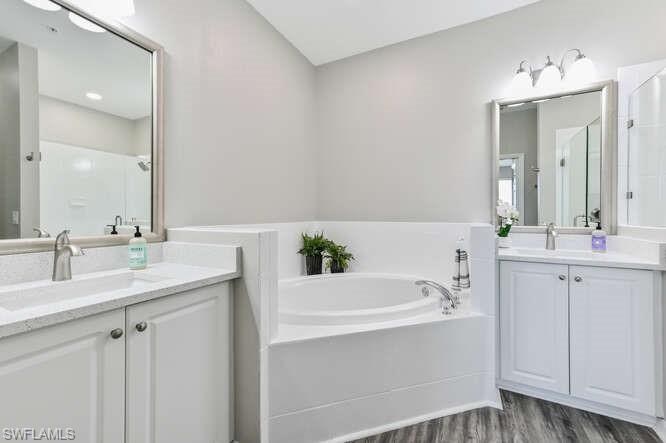 Bathroom with two vanities, a bath, a shower stall, and dark wood-style floors
